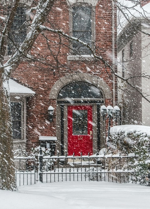 Bright red door on a brick house during heavy snowfall