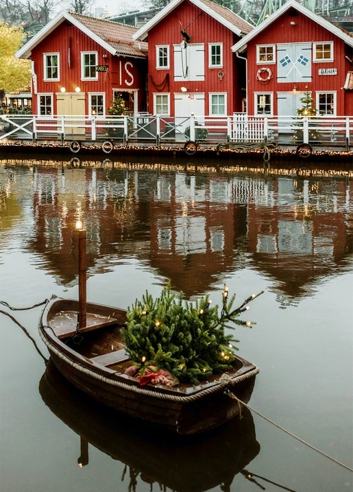 Rote Holzhäuser am Kanal mit einem Ruderboot und beleuchtetem Weihnachtsbaum