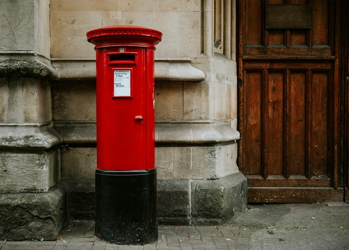Classic red pillar postbox on a weathered stone street corner beside a wooden door