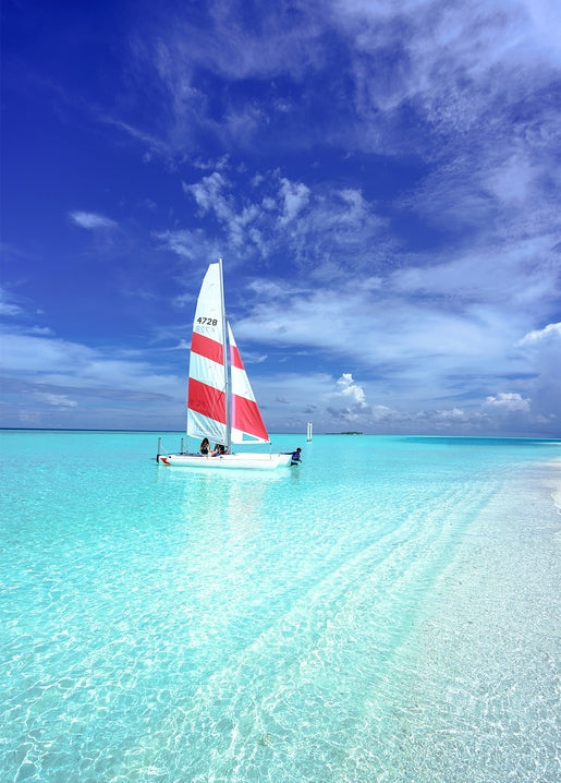 Small sailboat with red and white striped sail on shallow turquoise water