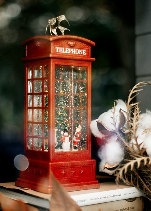 Red telephone booth snow globe with Christmas tree and Santa, surrounded by books and cotton branches