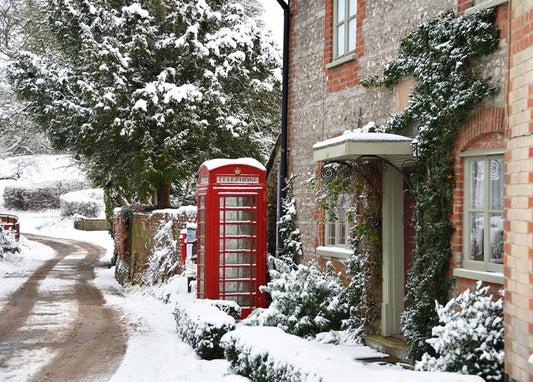 Red telephone box in snow beside an ivy-covered English cottage