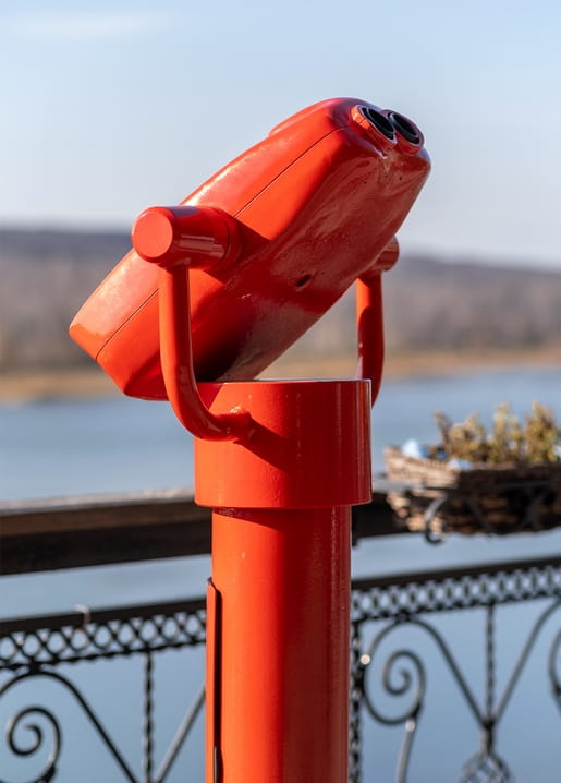 Red coin-operated telescope overlooking a river from an ornate iron railing