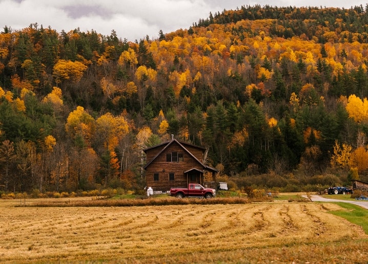 Roter Pickup vor einem Bauernhaus unterhalb eines herbstlichen Berghangs