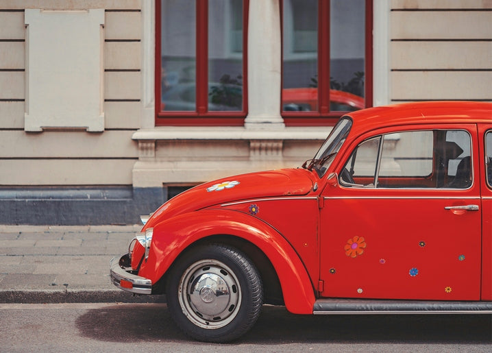 Glossy red Volkswagen Beetle with flower stickers parked in front of a townhouse with red windows