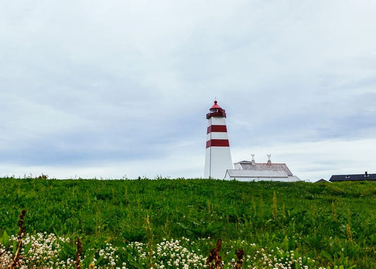 Red and white striped lighthouse on a grassy hill under cloudy sky