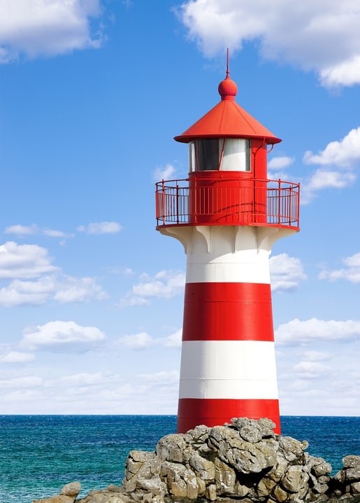 Red-and-white striped lighthouse standing on rocks by the sea