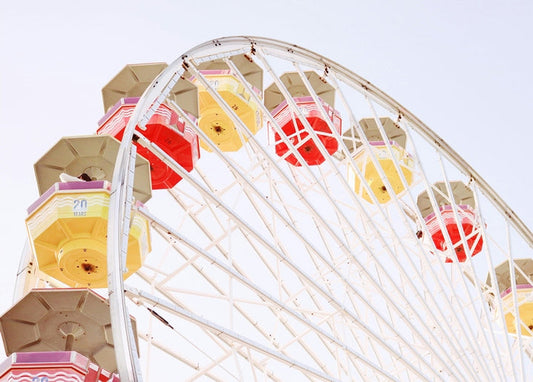 Red and yellow Ferris wheel against a pale summer sky, fairground postcard image
