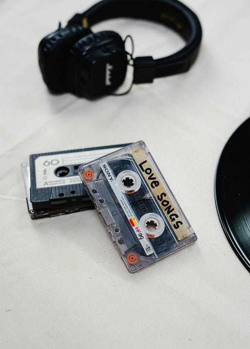 Two cassette tapes labeled 'Love Songs', headphones, and a vinyl record on a cream tablecloth