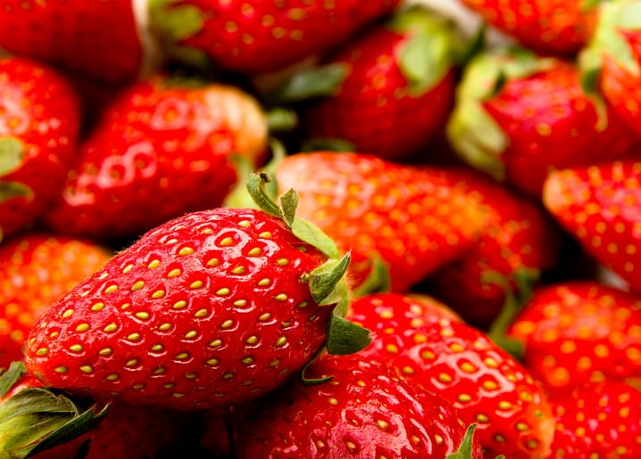 Close-up of glossy ripe red strawberries piled together, some sliced open