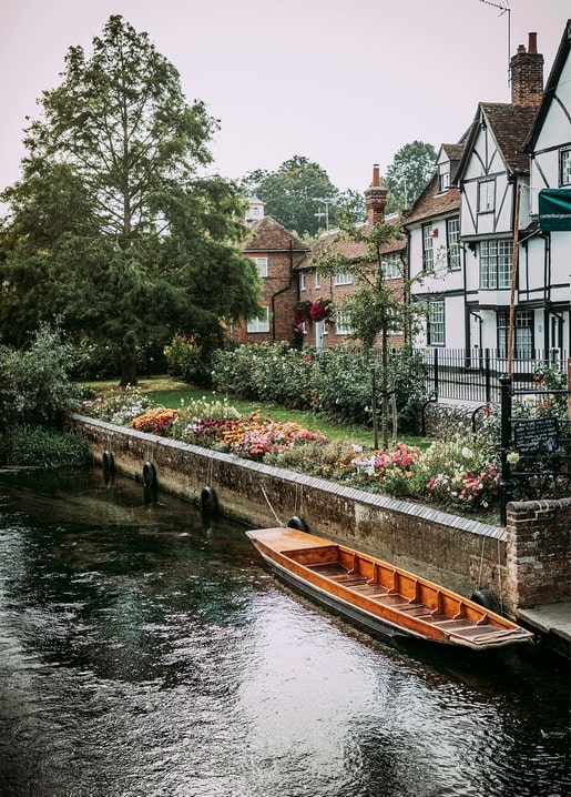 Holzboot auf einem Kanal neben Fachwerkhäusern und einem blühenden Blumenbeet