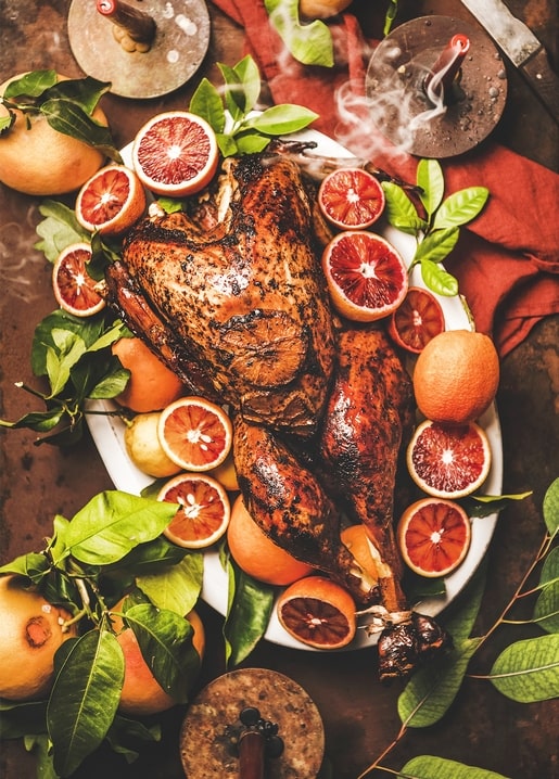 Whole roast bird surrounded by blood orange halves and citrus leaves on a platter
