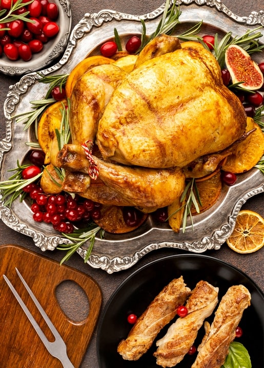 Golden roast turkey on a silver platter with cranberries, rosemary and orange