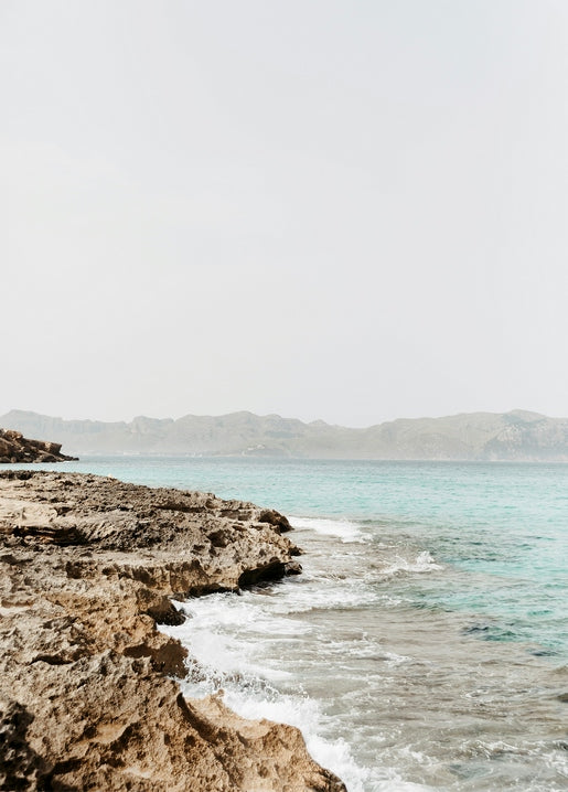 Rocky coastline with turquoise sea and hazy mountains in the distance