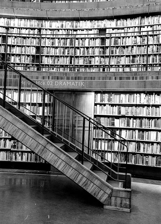 Gebogene Bibliotheksregale mit Holztreppe und einem Schild „Dramatik“
