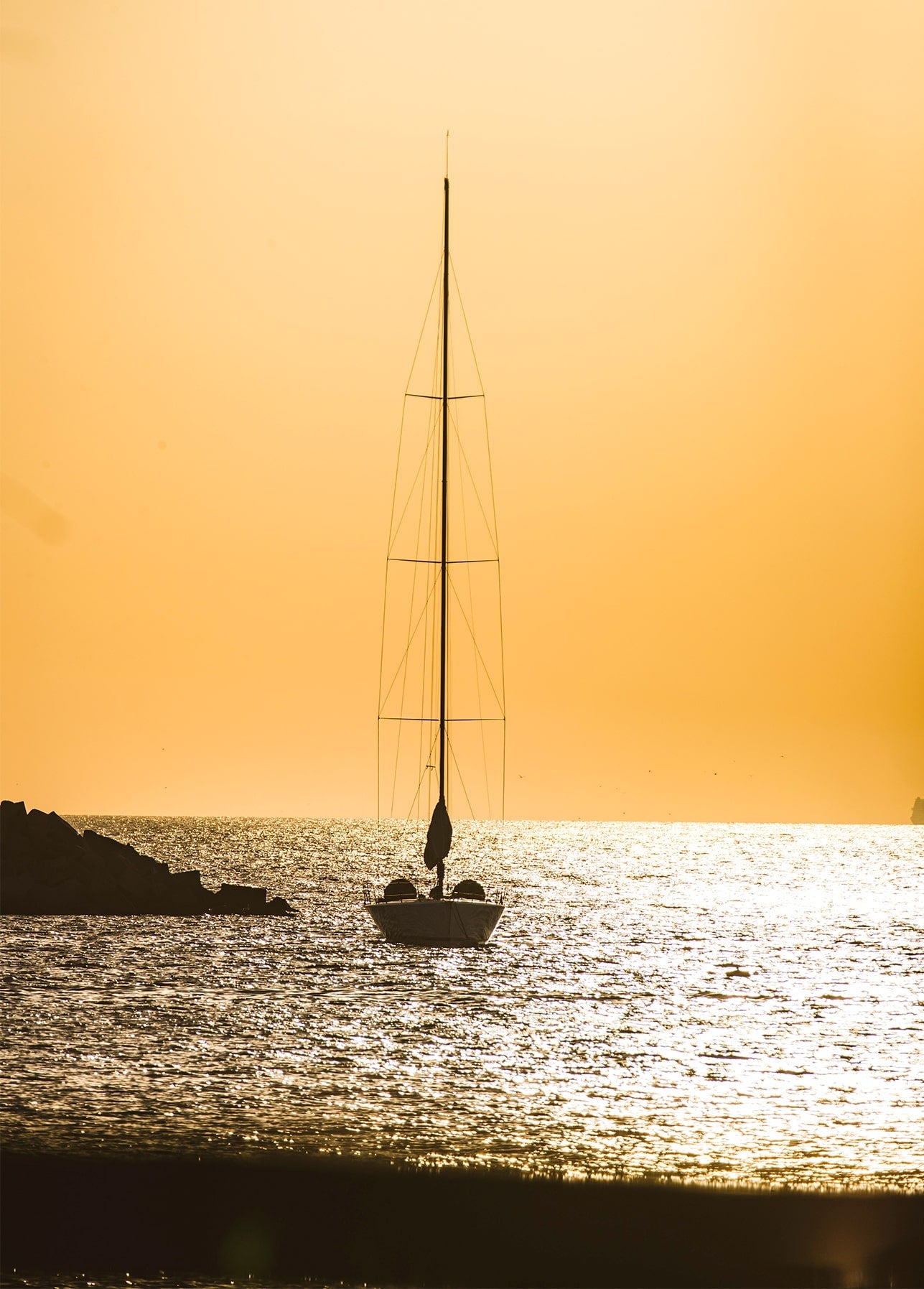 Silhouette eines Segelboots vor Anker bei goldenem Sonnenuntergang über dem Meer