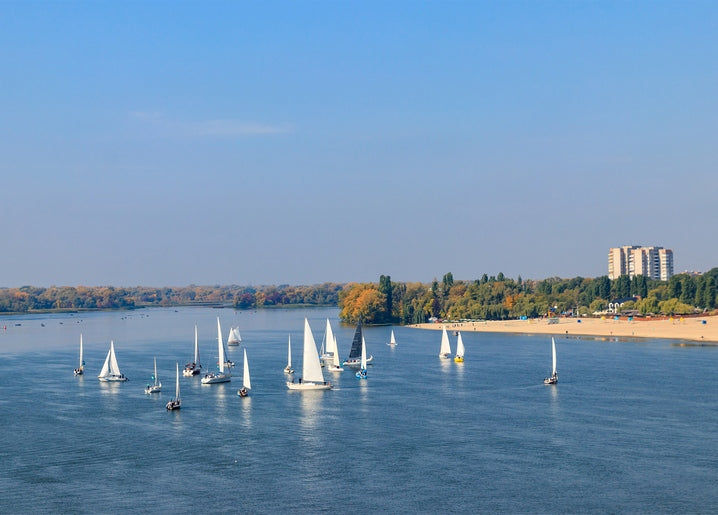 White sailboats racing on the Dnipro River near Kremenchuk's beach and skyline