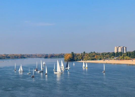 White sailboats racing on the Dnipro River near Kremenchuk's beach and skyline