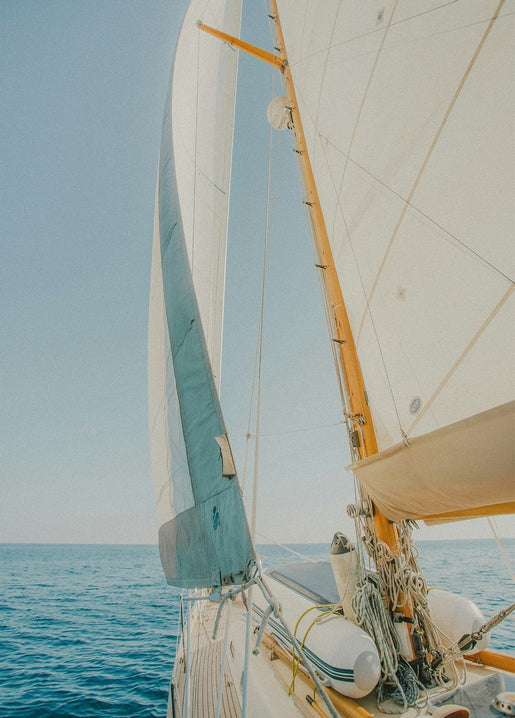 View from a sailboat's deck of white sails catching the wind over blue sea