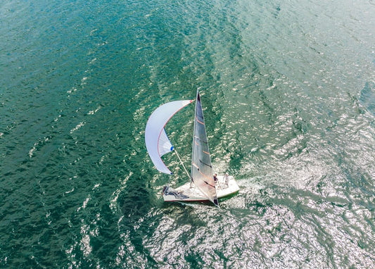 Segelboot mit Spinnaker auf türkisfarbenem Wasser aus der Vogelperspektive