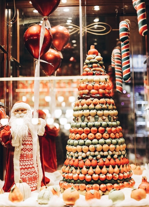 Santa Claus figure with balloons beside a pyramid of candied fruit in a Christmas shop window