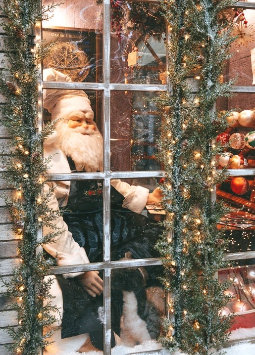 Vintage Santa Claus figurine glowing behind a frosted, garland-lit shop window
