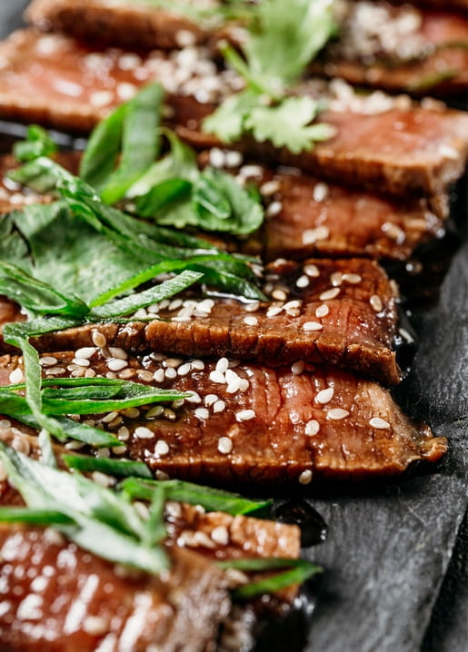 Close-up of sliced seared steak topped with sesame seeds and fresh herbs