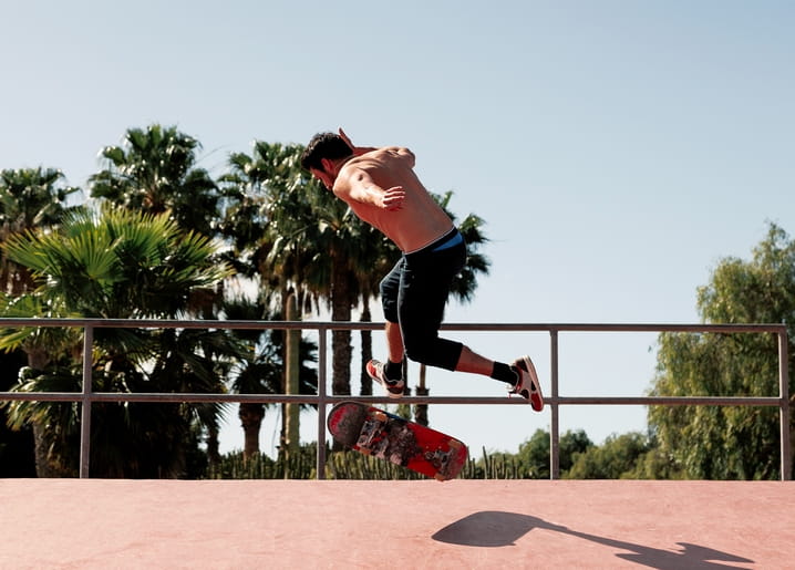 Skateboarder springt mit Trick vor Palmen im Skatepark