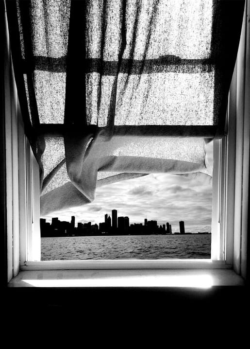 Transparenter Vorhang weht im Fenster vor einer Skyline über dem Wasser