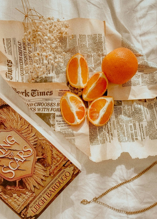 Sliced oranges, a paperback book, and dried flowers on a torn newspaper