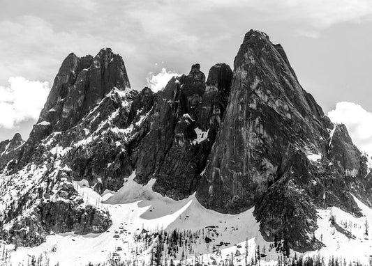 Jagged snow-capped mountain peaks rising above a forested valley under a cloudy sky