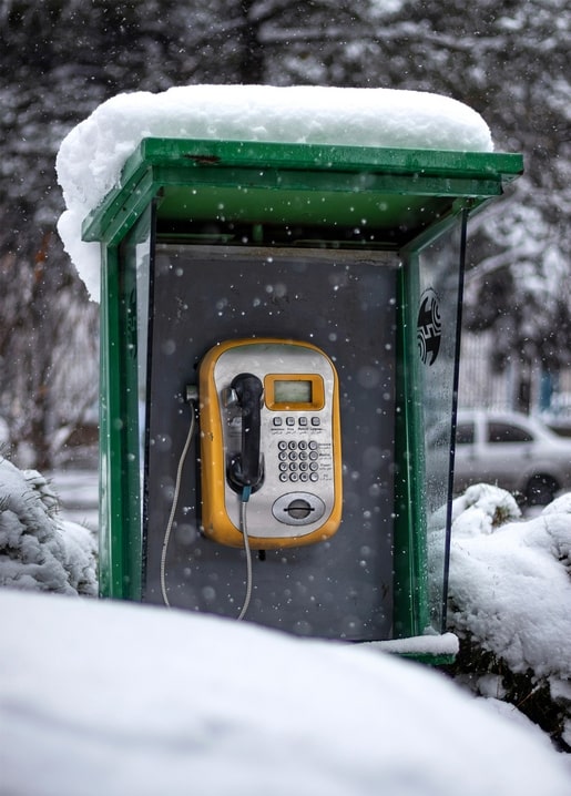 Green payphone booth covered in snow with falling snowflakes on a winter street