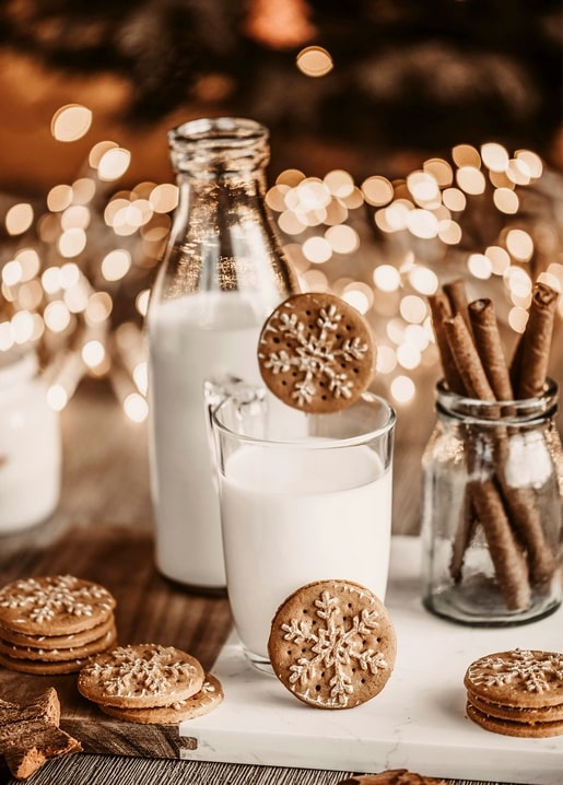 Snowflake-shaped cookies, a glass of milk and glowing fairy lights on a table