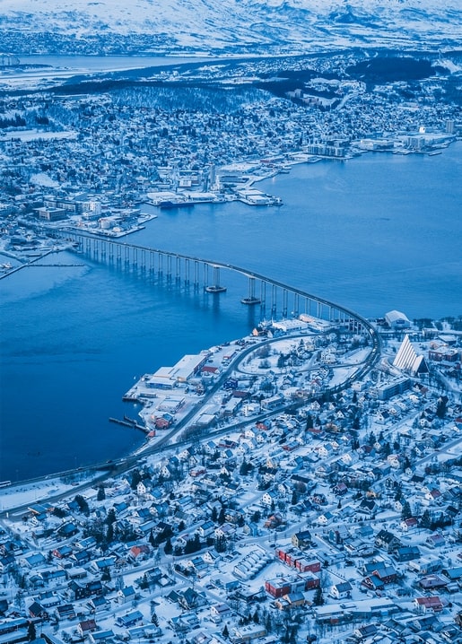 Aerial view of a snow-covered coastal town with a long bridge across a fjord
