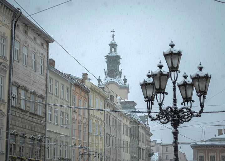 Schneebedeckte, verzierte Laterne auf einer historischen Straße in Lviv vor einem Kirchturm