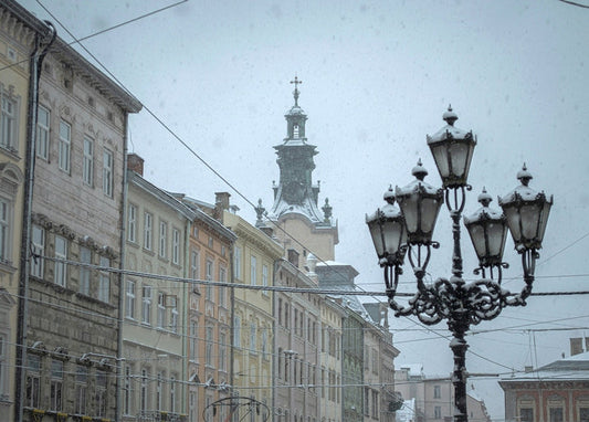Snow-covered ornate lamppost on a historic Lviv street with a church tower in the background