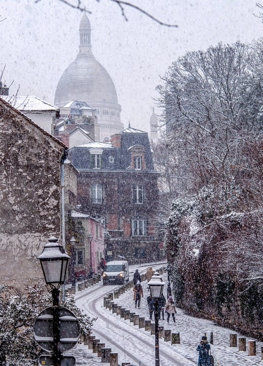 Snowy staircase street in Montmartre, Paris, with the Sacré-Cœur dome in the distance