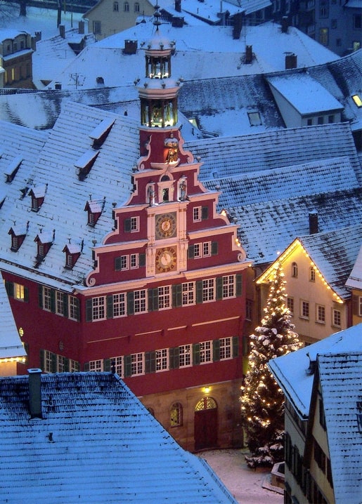 Snow-covered old town rooftops with an ornate red bell tower glowing at dusk