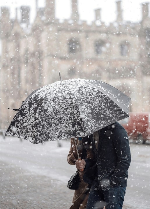 Couple walking under a snow-covered umbrella near an old stone building