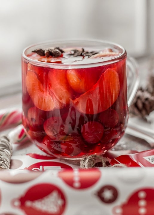 Glass mug of spiced fruit punch with cherries and orange slices beside a candy cane