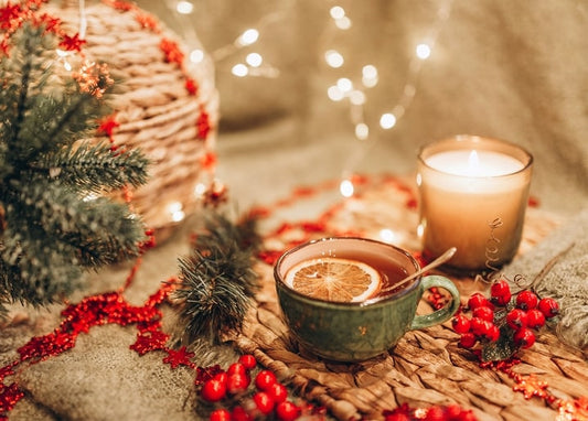 Mug of spiced tea with orange slice beside a candle and fairy lights
