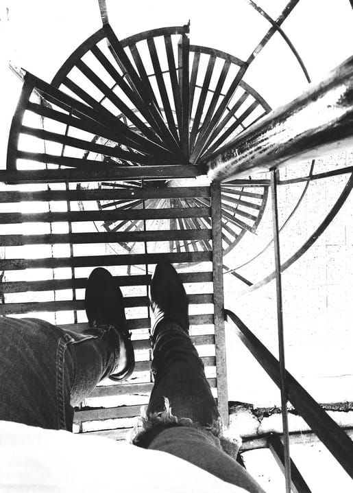 Looking straight down a spiral iron staircase with shoes visible in the foreground