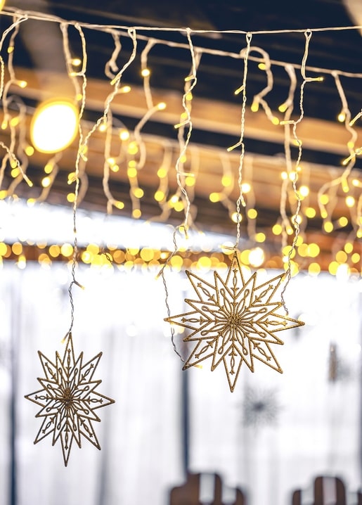Two glittering star ornaments hanging among warm icicle fairy lights