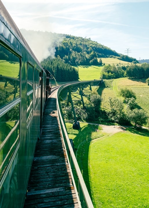 Green steam train crossing a wooden viaduct above green hills