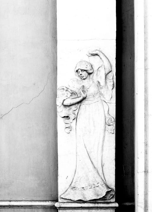 Steinrelief einer Frau im Gewand mit erhobenem Arm, die ein Kind an sich drückt.