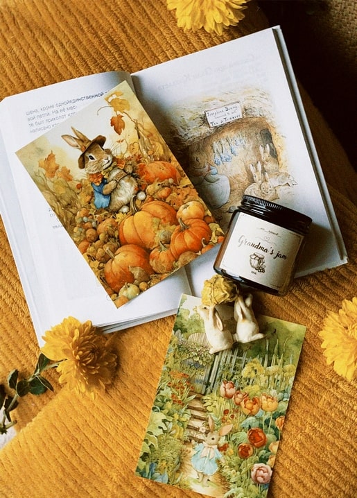 Aufgeschlagenes Bilderbuch mit Kaninchen-Illustrationen neben einem Marmeladenglas und Chrysanthemen