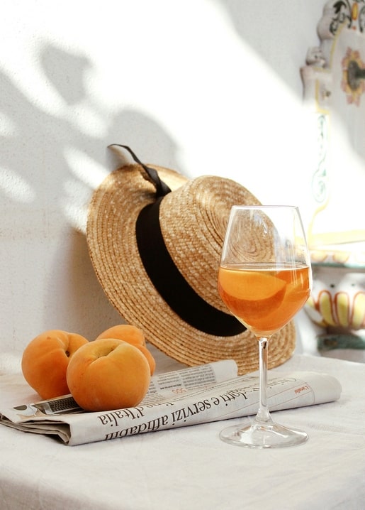Straw hat, glass of wine and ripe apricots on an Italian newspaper in sunlight