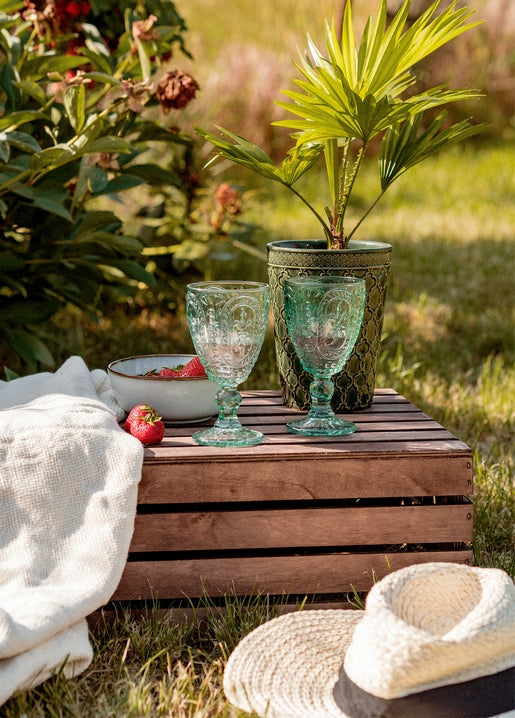 Etched wine glasses, strawberries and a straw hat on a wooden crate in a summer garden