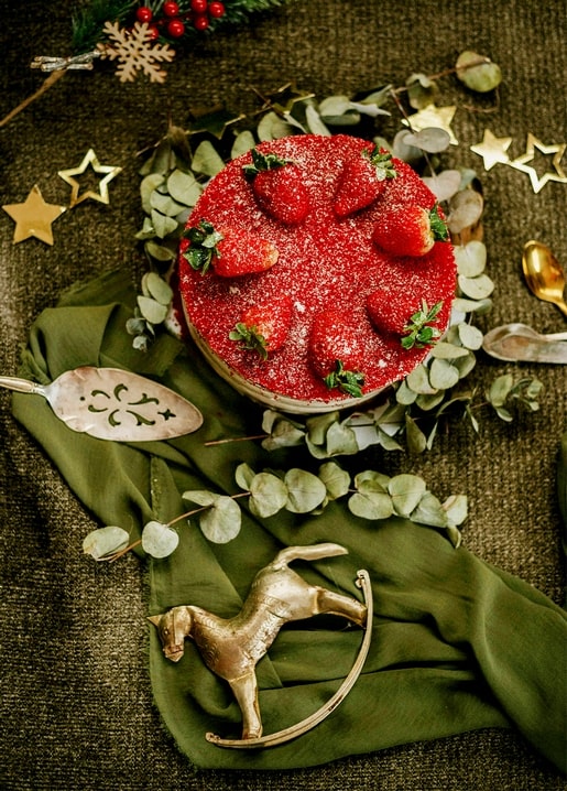 Overhead view of a strawberry Christmas cake in a eucalyptus wreath with gold star ornaments and a brass reindeer