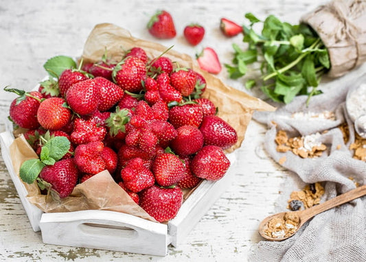 Wooden crate of fresh strawberries with mint and granola on linen cloth